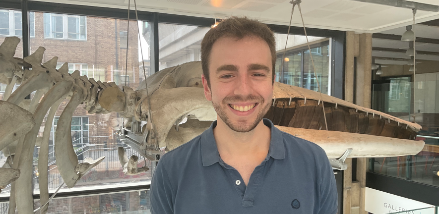 Alex Almeida stood smiling in front of a whale skeleton