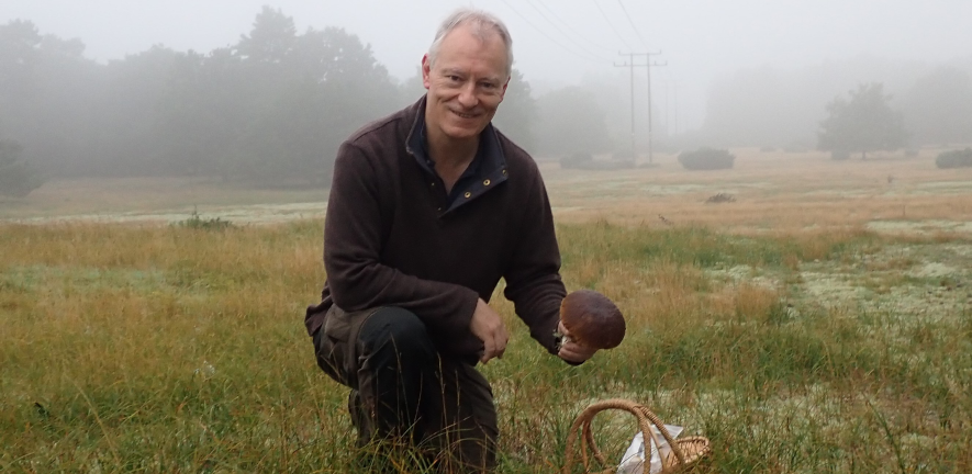 William Amos kneeling in a field holding a mushroom