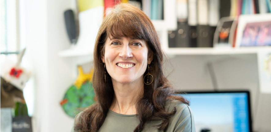 A head and shoulders photo of Andrea Brand, smiling, standing in a laboratory with a blurred background