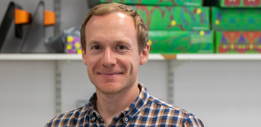 James Edgar, smiling, wearing checked shirt, standing in a laboratory