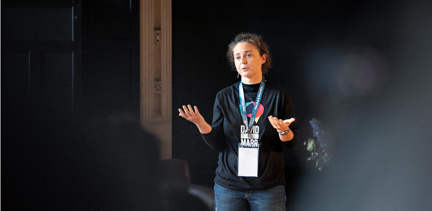 Photo of Elisa Galliano in a dark shirt presenting at a conference 