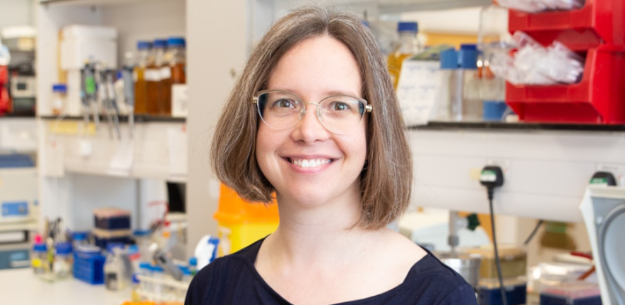 Jenny gallop, in a blue top, in front of a blurred laboratory background