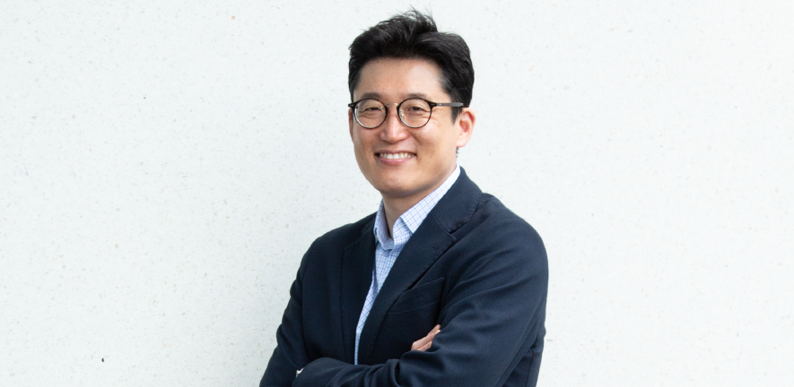 Namshik Han, stood in a suit with arms crossed against a white background