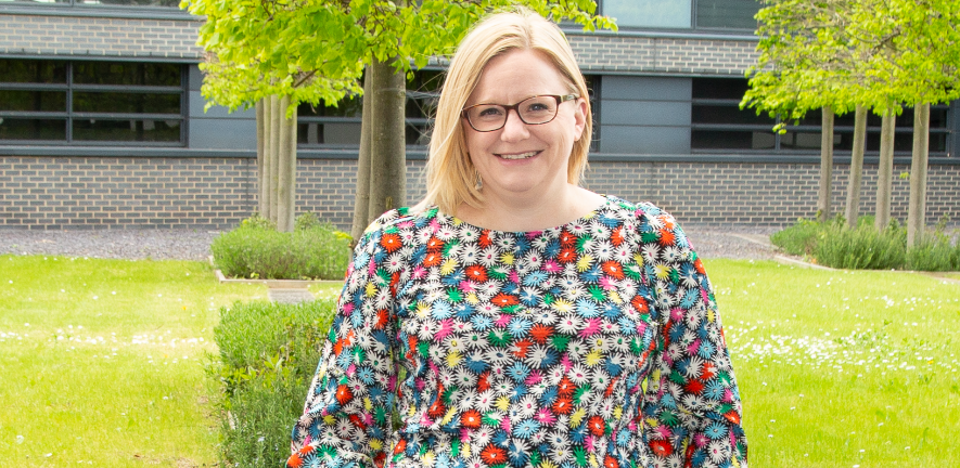 Rebecca Harris in a floral shirt sat on a wall in a garden 