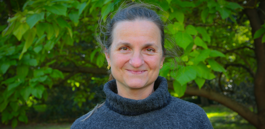 Claire Hughes in a grey turtleneck standing in front of a tree