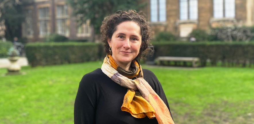 Adria LeBouef, smiling, in grassy courtyard, wearing black top with orange scarf