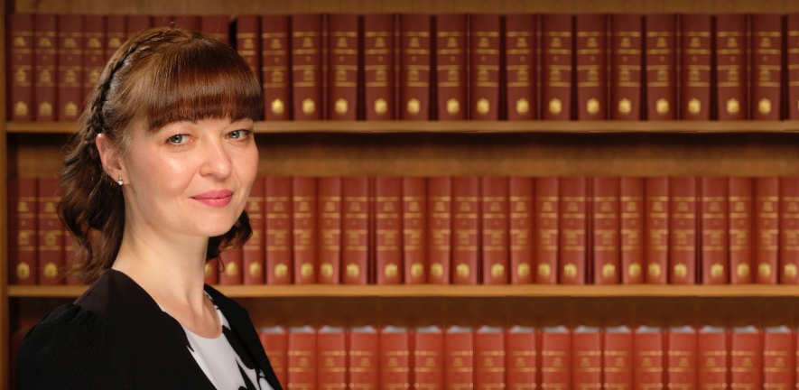 Valeria Lulla in a black gown standing in front of a bookcase 