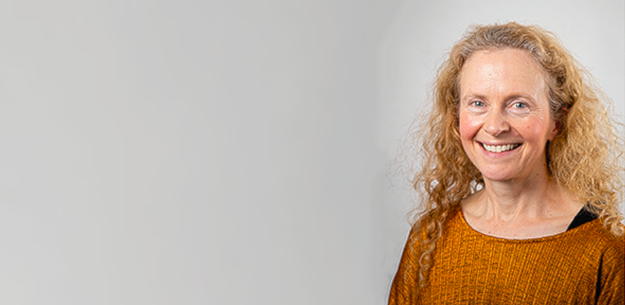 Laura Machesky, smiling in orange top against grey background 