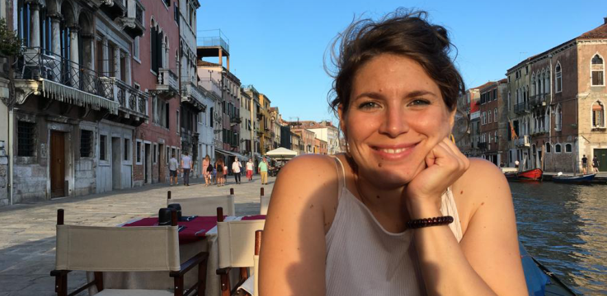 Elena scarpa, sitting at a restaurant table outside by a canal, smiling 