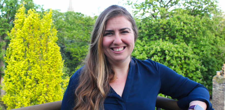 Alecia-Jane Twigger, smiling, on a balcony against a backdrop of trees