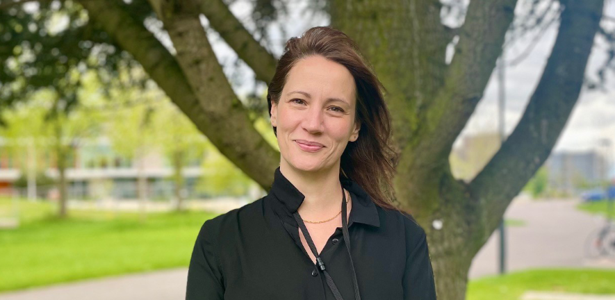 Lucy Weinert, smiling, in black blouse on windy day standing in front of a tree