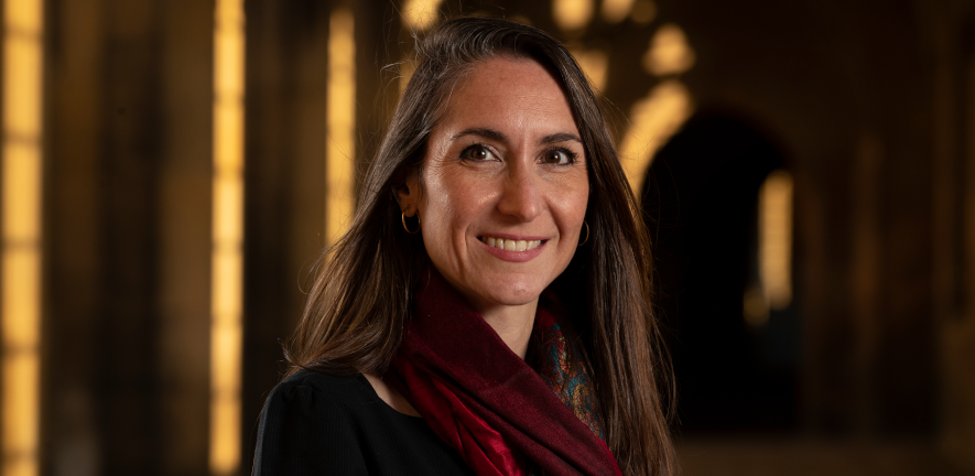 Amanda Sferruzzi-Perri. Photo credit Chris Radburn/Fixed Point Media Amanda Sferruzzi-Perri, smiling, wearing a red scarf, standing in stone corridor with sunlit background