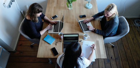 3 women sitting at a table working on laptops