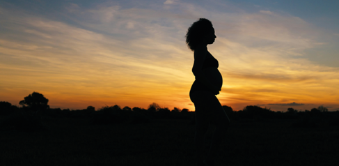 Pregnant woman standing with sunset behind