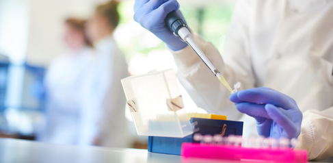researcher sitting at a lab bench using a pipette to transfer samples