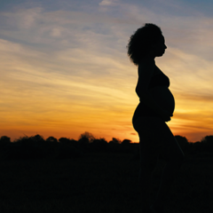 Pregnant woman standing with sunset behind