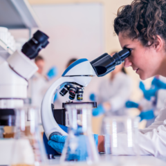 woman wearing a lab coat looking into a microscope