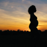 Pregnant woman standing with sunset behind