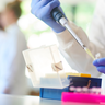 researcher sitting at a lab bench using a pipette to transfer samples