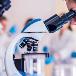 woman wearing a lab coat looking into a microscope