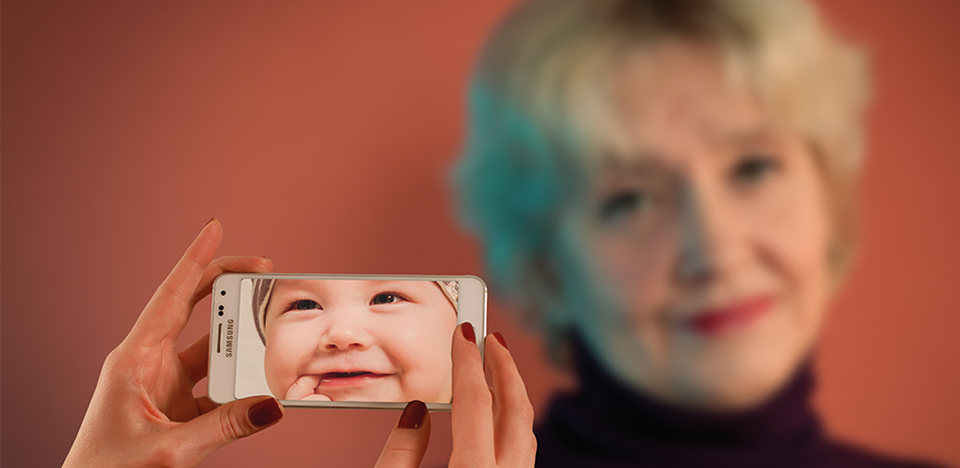 hands holding smartphone with photo of baby with older woman in the background