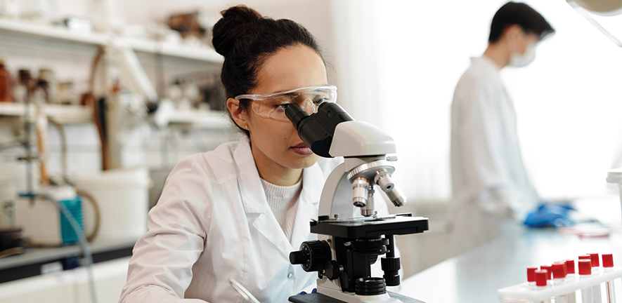 woman in lab looking through microscope